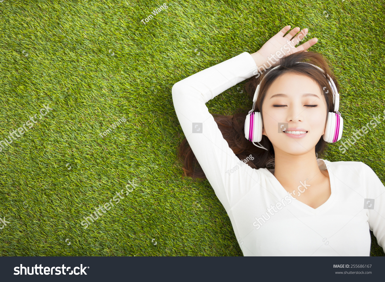 轻松的女人戴着耳机听音乐,躺在草地上-背景\/素